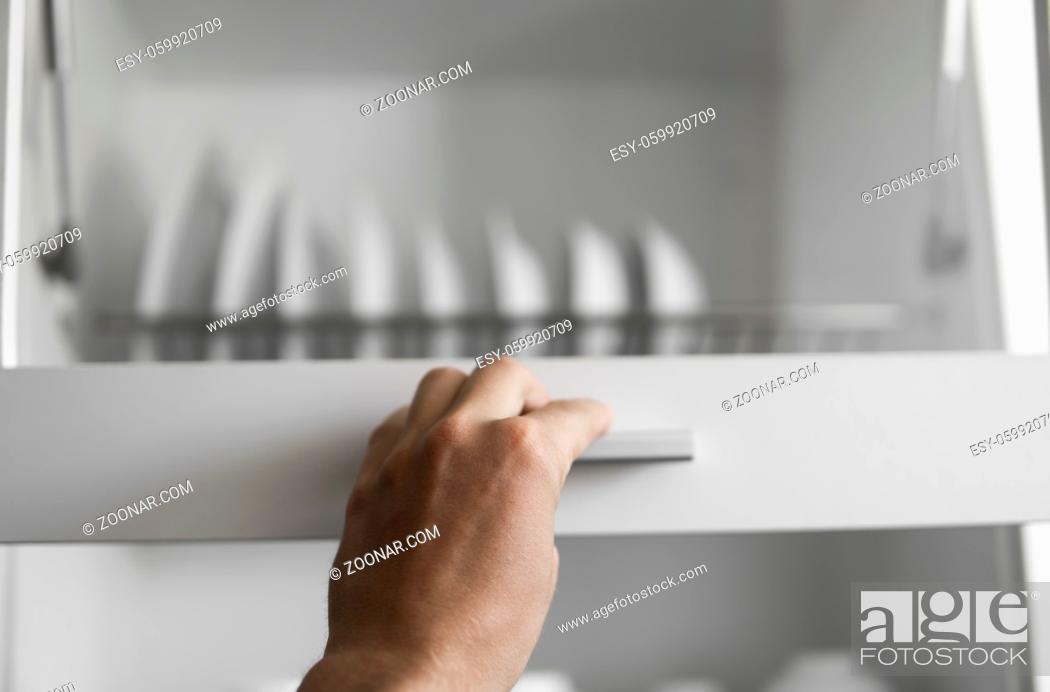 Stock Photo: Hand holds the door of the dryer with utensils. Dish drying metal rack with white clean plates. Traditional comfortable kitchen.