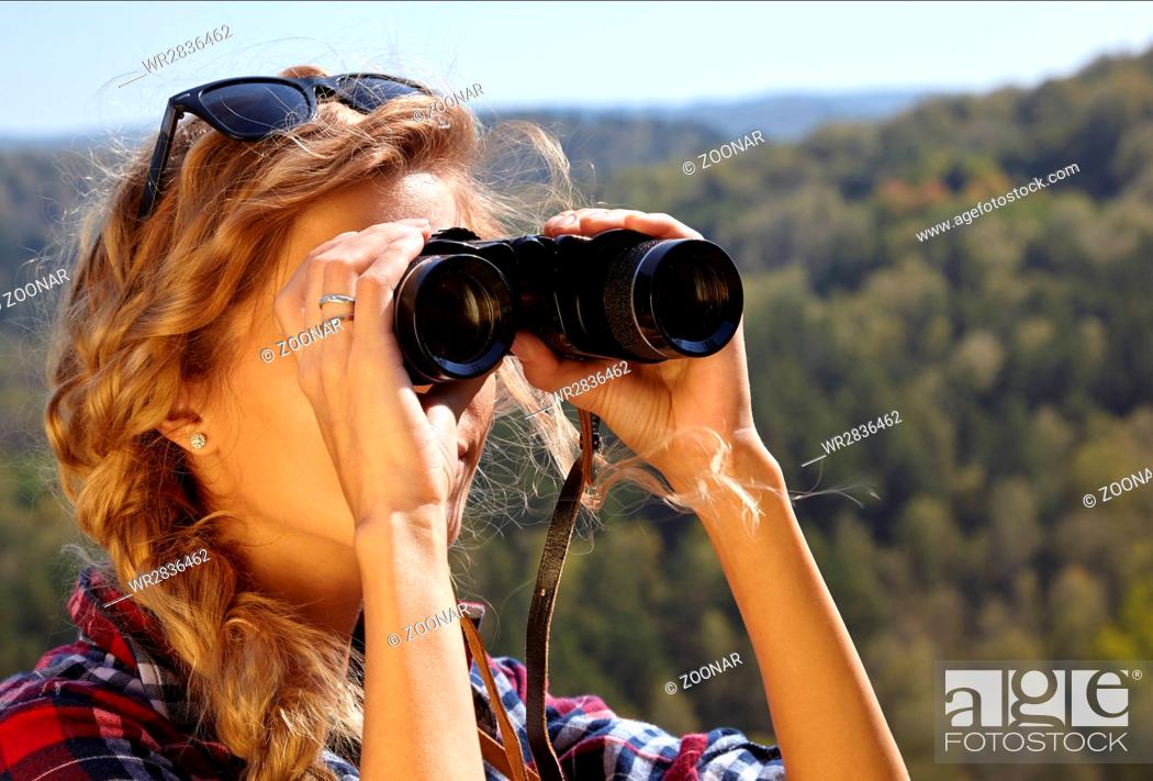 Imagen: Young blonde woman tourist  on a cliff looking through binoculars on the autumn landscape.