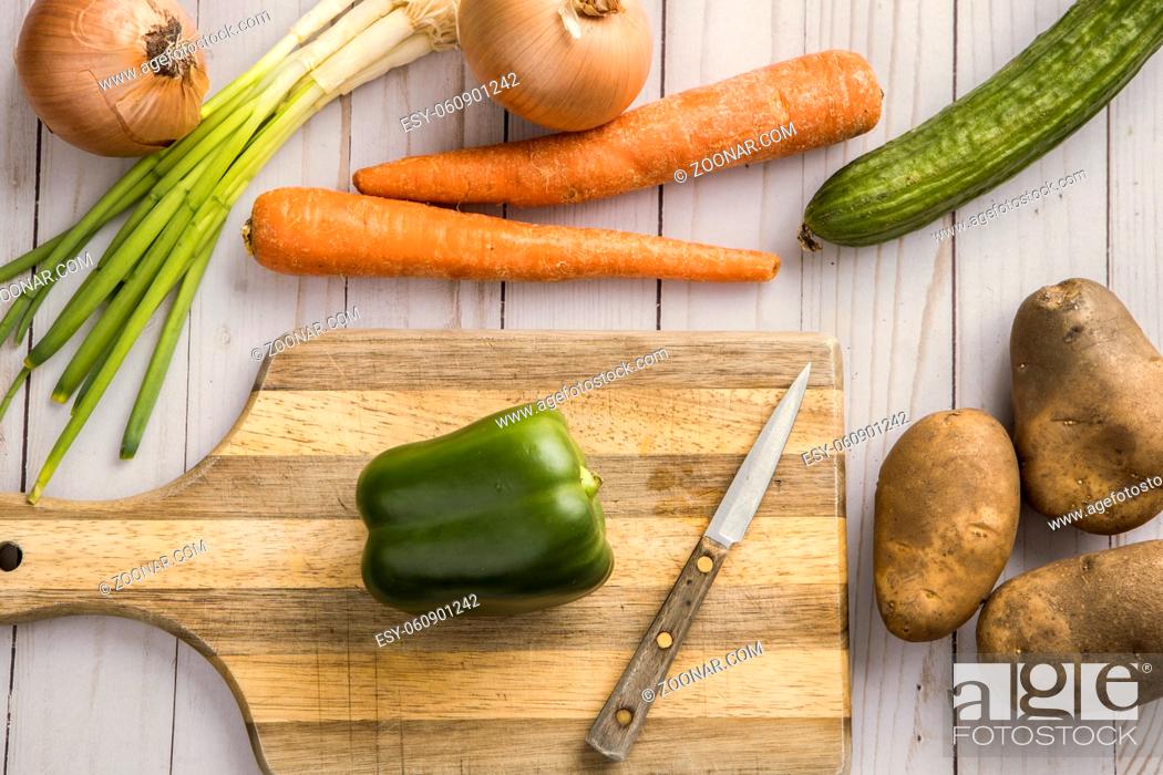 Stock Photo: An assortment of vegetables such as onions, carrots, potatoes, and green bell pepper and a cutting board.