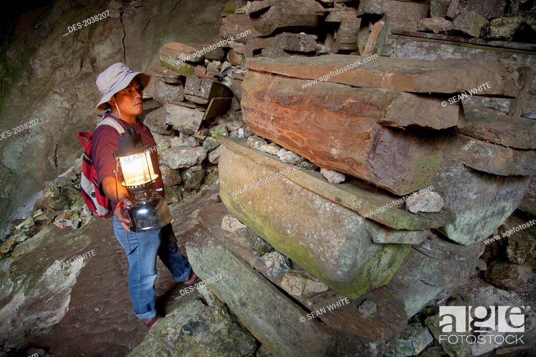 Stock Photo: A Tour Guide Uses A Lantern To Look At The Many Coffins In The Entrance To Lumiang Burial Cave Near Sagada, Luzon Philippines.