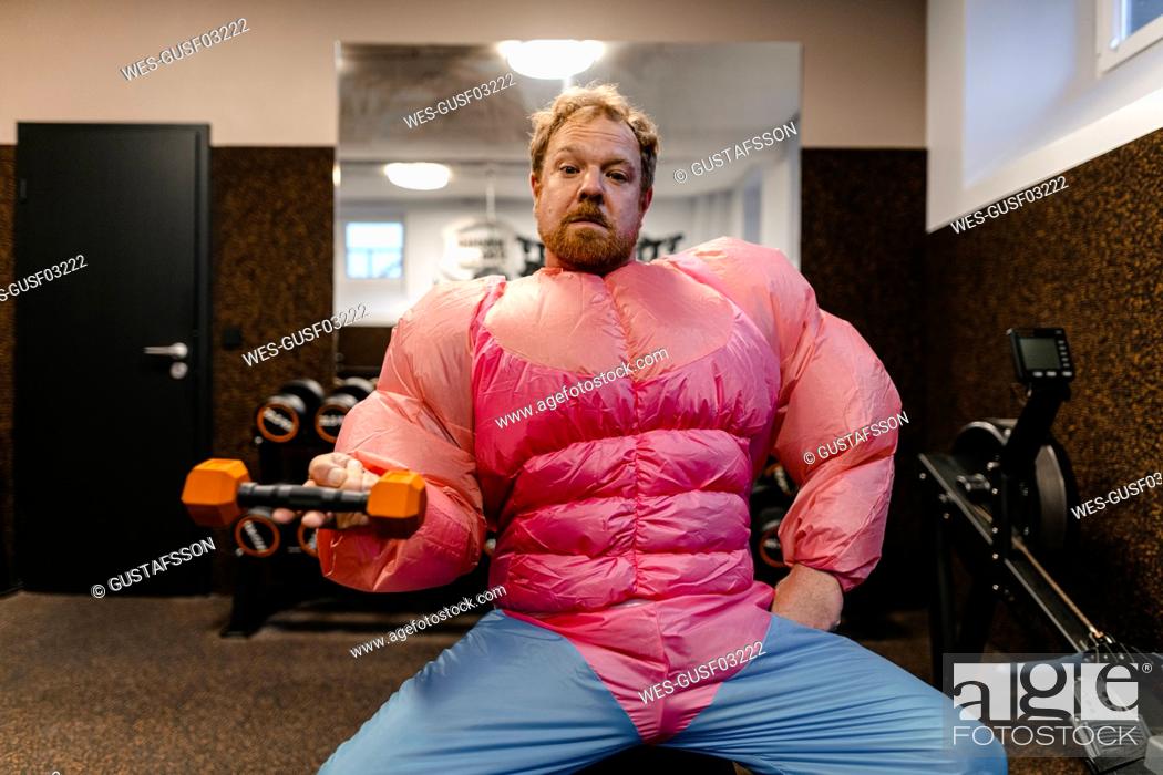 Stock Photo: Man in gym wearing pink bodybuilder costume lifting dumbbell.
