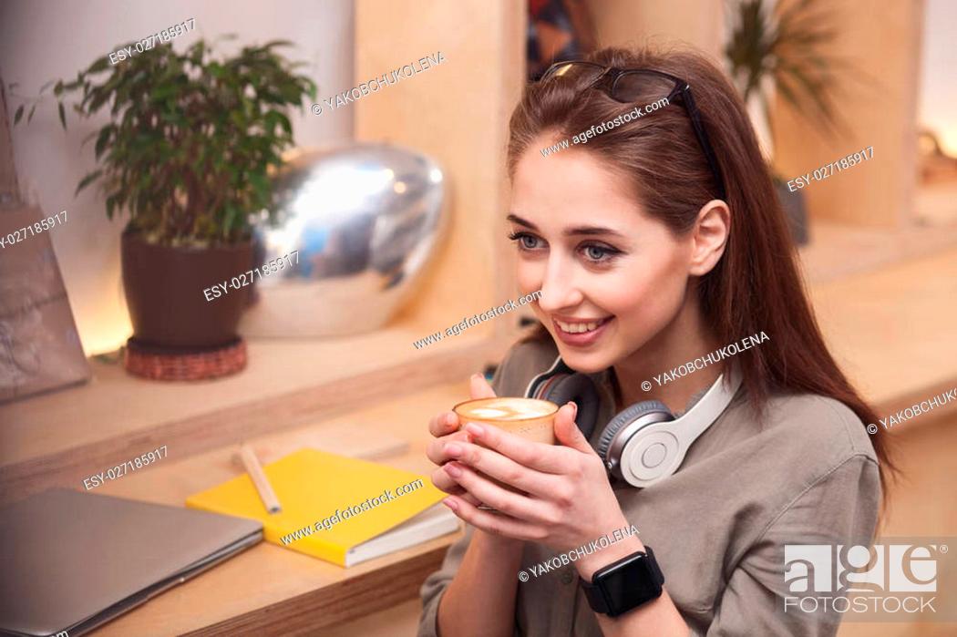 Stock Photo: Attractive girl is enjoying a cup of latte. She is sitting and smiling happily.