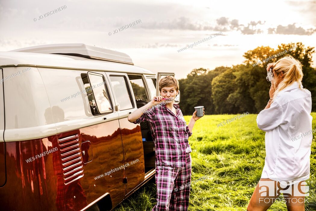 Stock Photo: Woman taking picture of friend brushing teeth at a van in rural landscape.