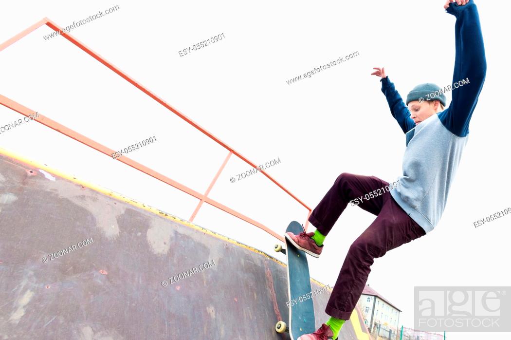 Imagen: Teen skater in a hoodie sweatshirt and jeans slides over a railing on a skateboard in a skate park, Wide angle.