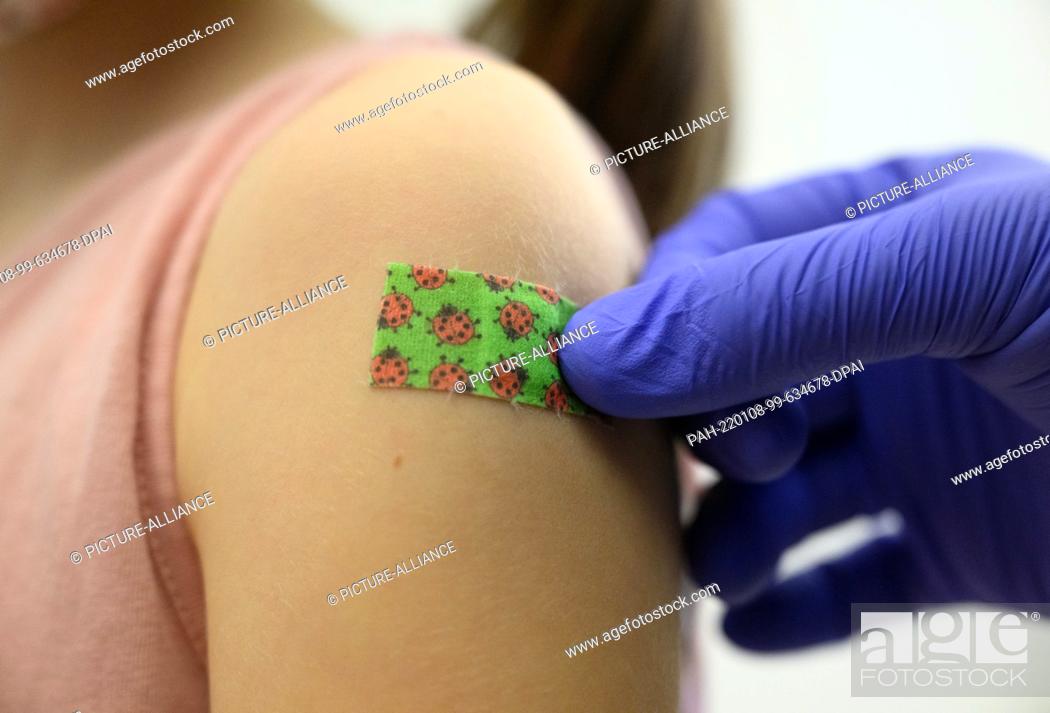 Stock Photo: 08 January 2022, Saxony, Dresden: A seven-year-old girl gets a plaster stuck on her arm after being vaccinated against the coronavirus during a vaccination.