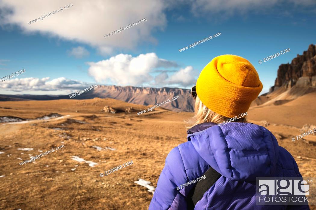 Photo de stock: Close-up Portrait from the back of a girl traveler in a jacket with a cap and a backpack stands on the background of an epic landscape with rocks.