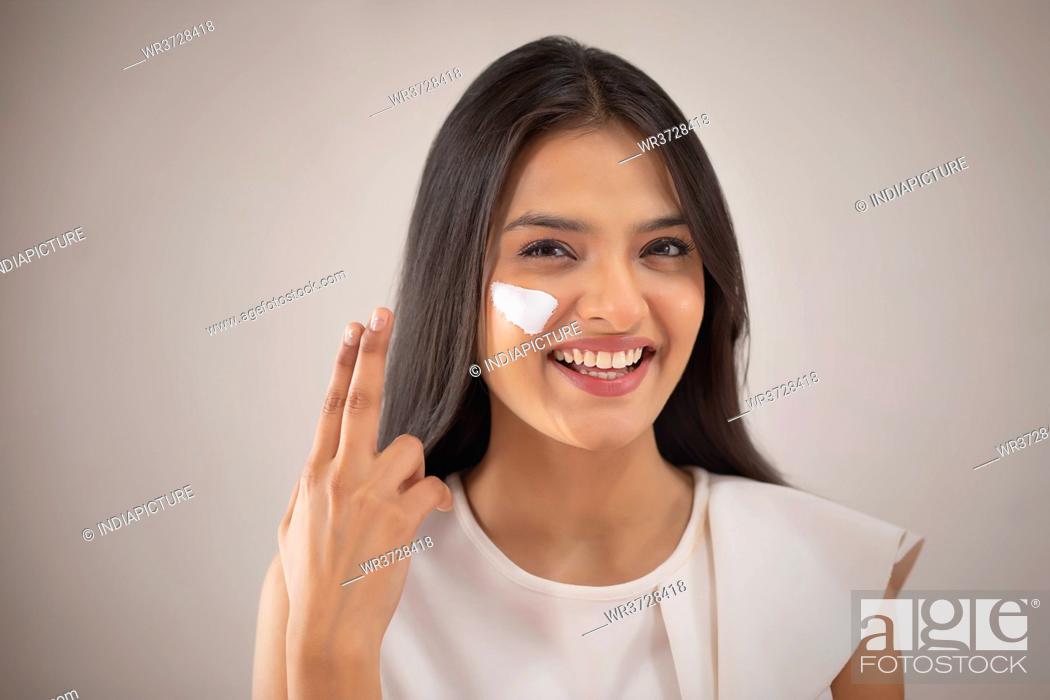 Stock Photo: A CHEERFUL YOUNG WOMAN PUTTING CREAM ON FACE.