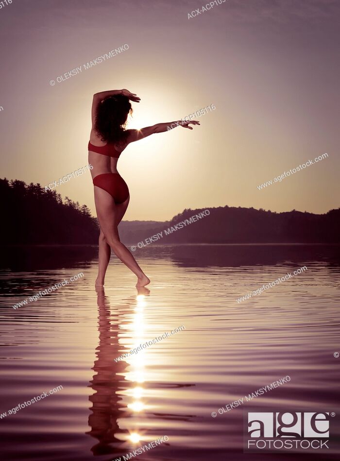 Stock Photo: Young woman in swimsuit dancing in the sun on the water in beautiful morning sunrise scenery. Muskoka, Ontario, Canada.