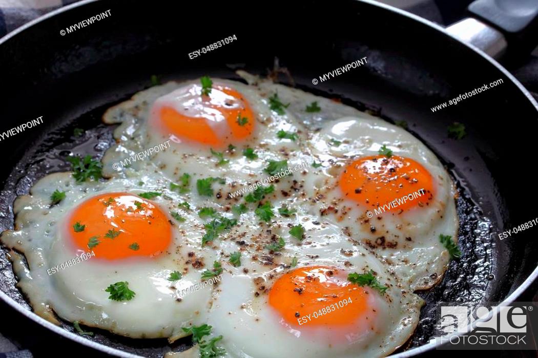 Stock Photo: savory hot fresh fried sunny side up eggs sprinkled with ground black pepper and finely chopped parsley in skillet on wooden table, view from above, close-up.