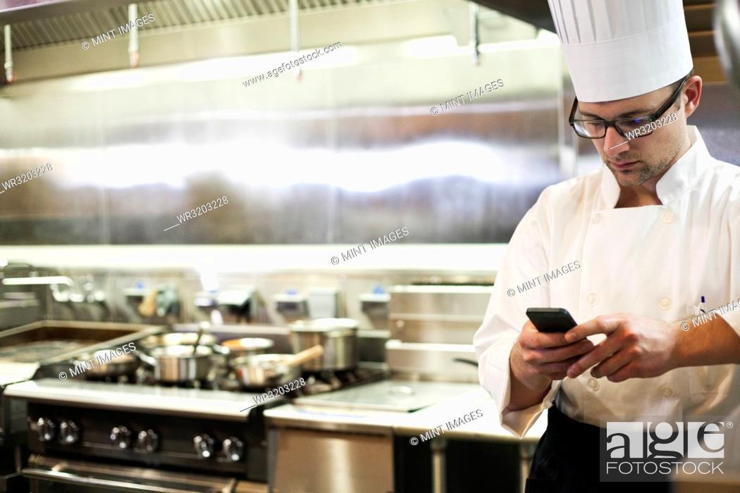 Stock Photo: A Caucasian male chef checking his cell phone in a commercial kitchen,.