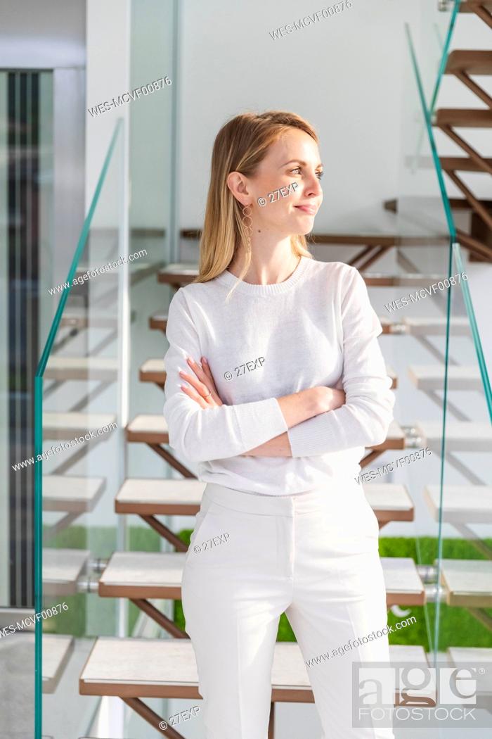 Stock Photo: Smiling female entrepreneur with arms crossed standing in front of steps at office.