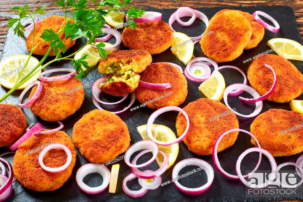 Stock Photo: delicious crispy rice patties with crumbled paneer cheese and finely chopped greens on a black slate plate with lemon slices and onion rings on wooden table.