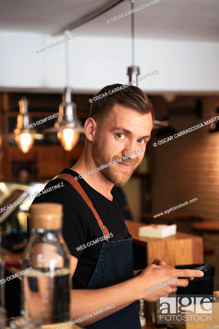 Stock Photo: Portrait of smiling barista using mobile phone in coffee shop.