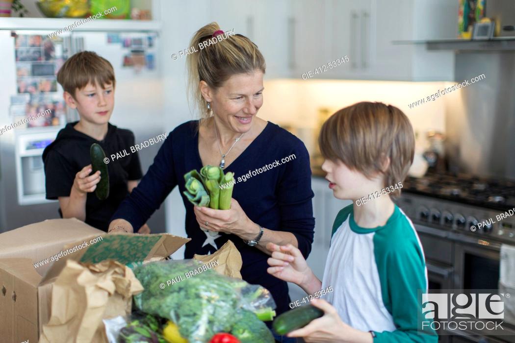 Stock Photo: Happy mother and sons unloading fresh produce from box in kitchen.