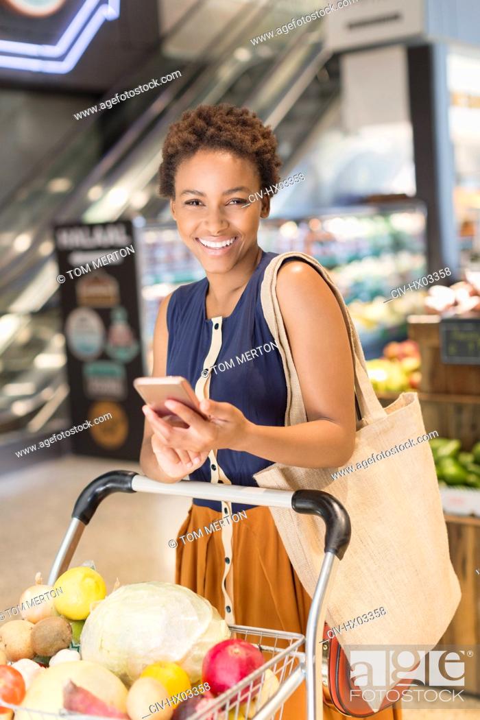 Stock Photo: Portrait smiling young woman using cell phone, grocery shopping in market.