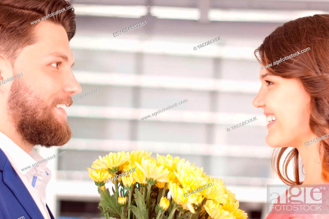 Stock Photo: Soft glance. Young smiling man giving some beautiful flowers to his lovely girlfriend.