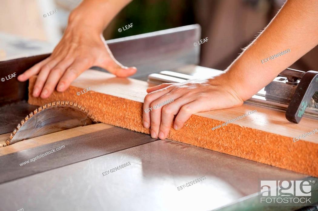 Stock Photo: Closeup of carpenter's hands cutting wood with tablesaw in workshop.