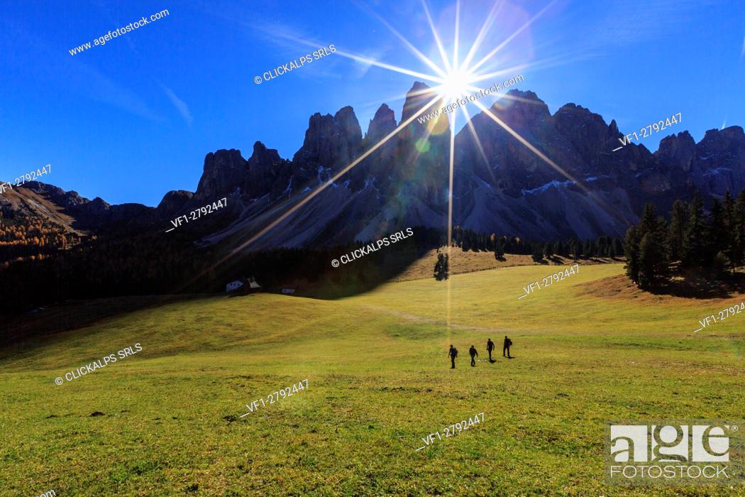 Stock Photo: Hikers crossing the green pastures of Malga Glatsch illuminated by sunbeams. Funes Valley South Tyrol Dolomites Italy Europe.