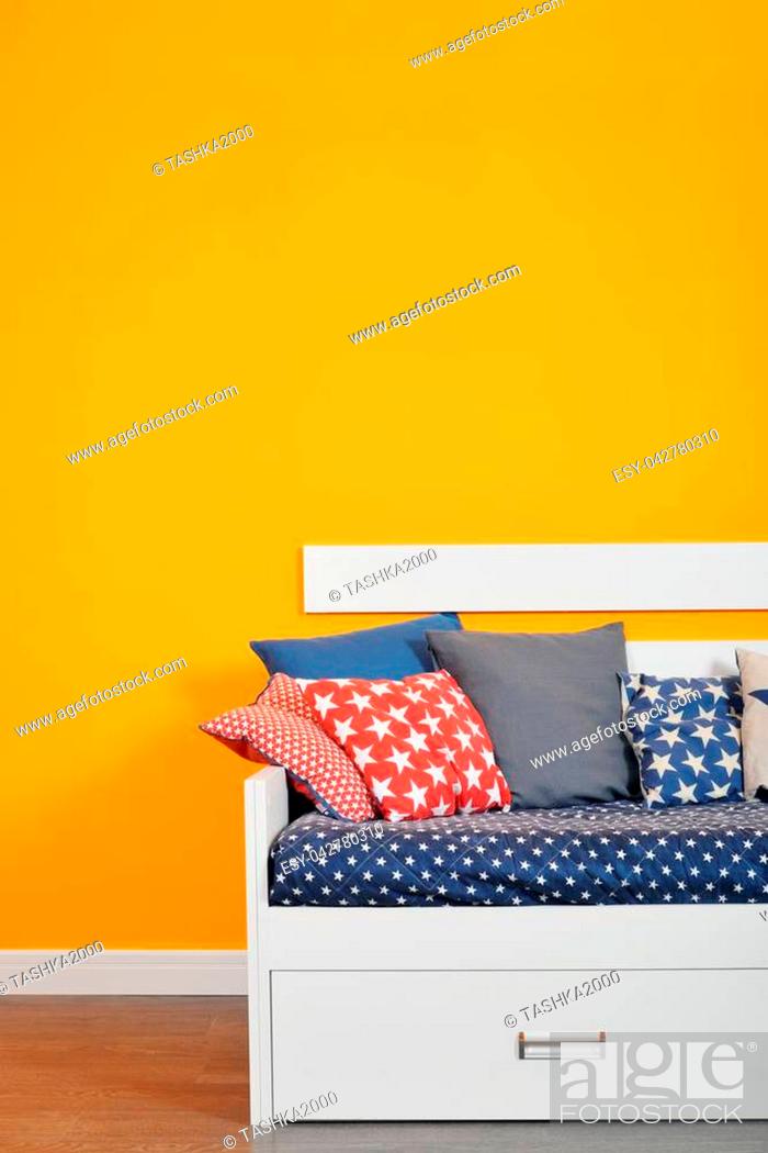 Stock Photo: Children's bed bed with different color pillows against orange wall in the room.