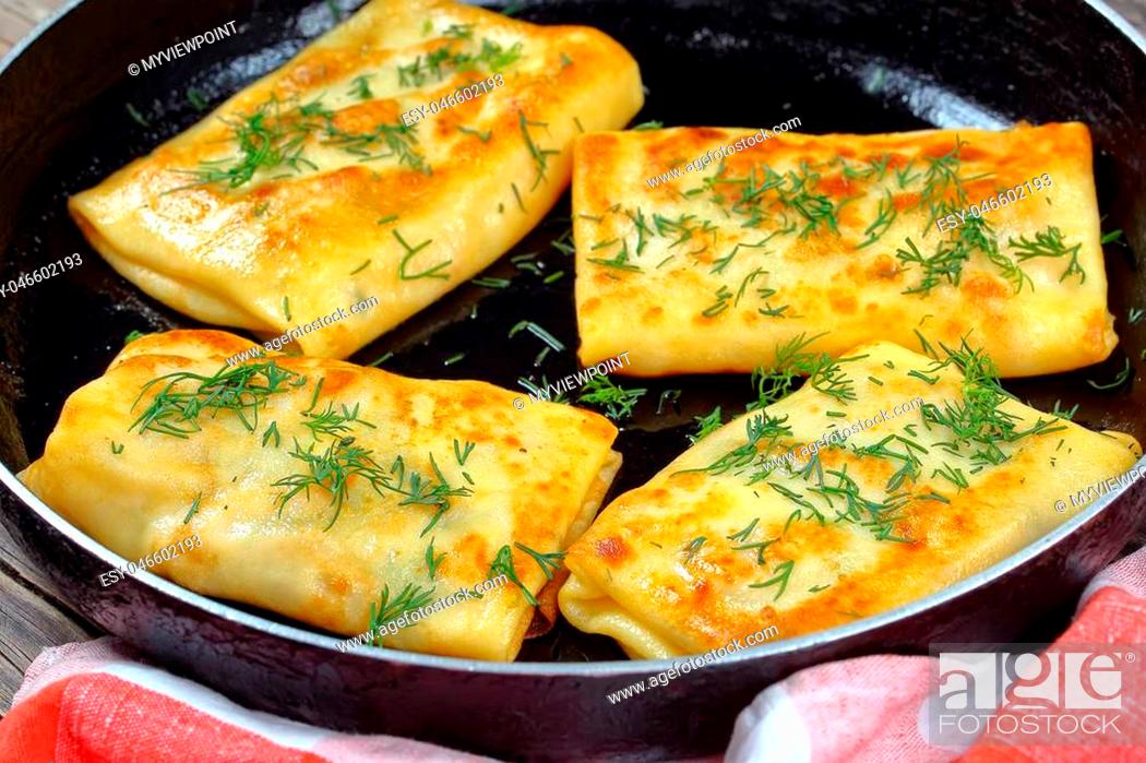 Stock Photo: delicious mozzarella stuffed crepes wraps on skillet sprinkled with finely chopped dill, on dark wooden board, view from above, close-up.