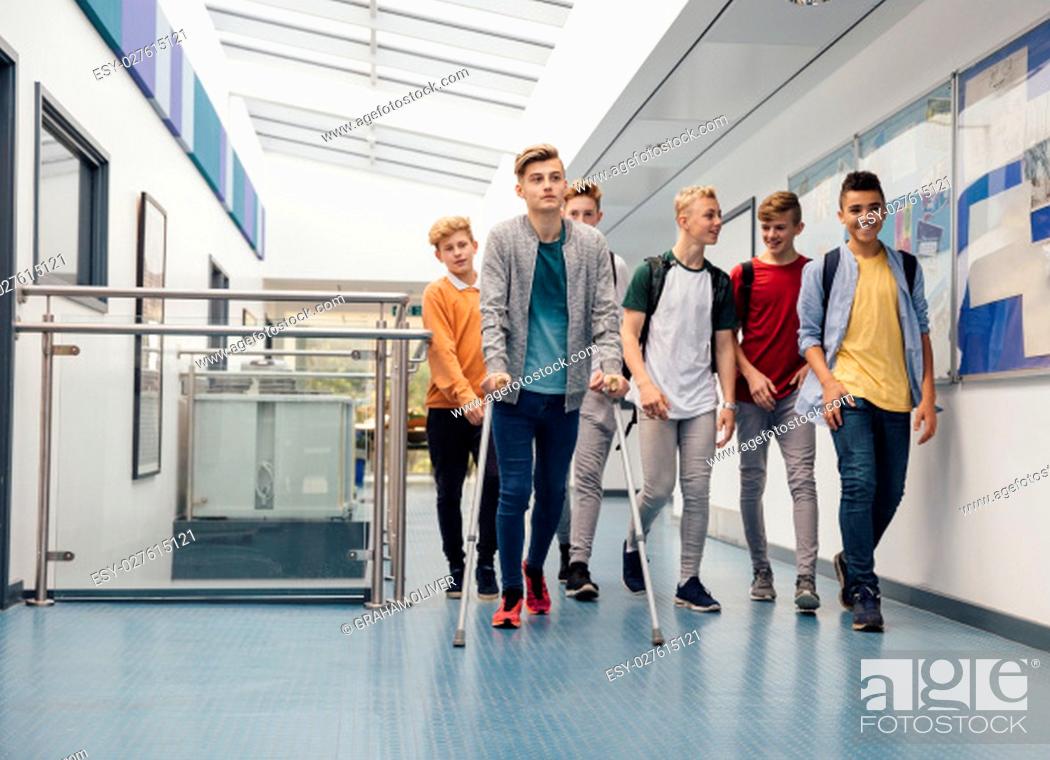 Stock Photo: Group of teenage boys are walking to their next school lesson together. They are talking and laughing as they walk and one of the students is using crutches.
