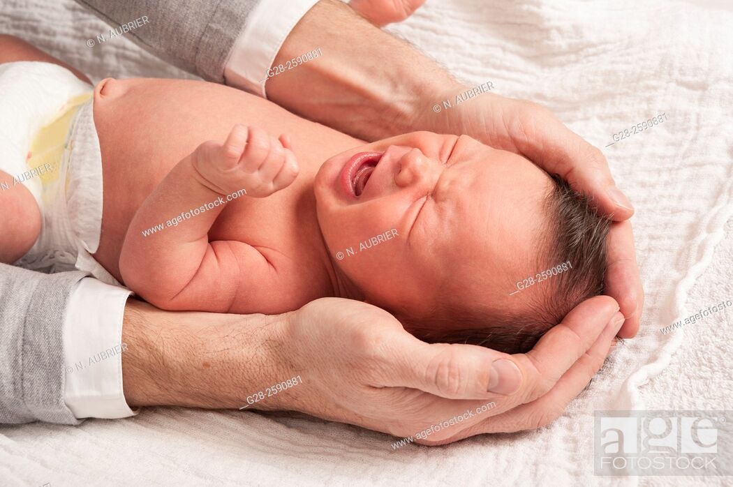 Stock Photo: Little baby boy crying, 2 weeks old, between his father's arms and hands, trying to soothe him, and protect him;.