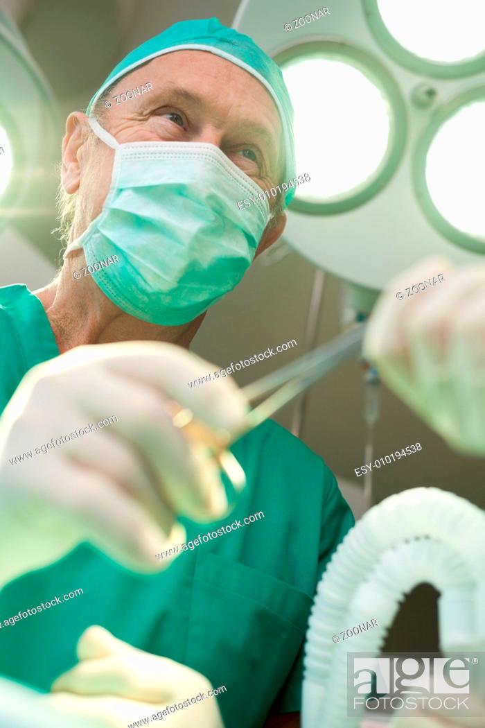 Stock Photo: Surgeon smiles as he takes a surgical scissors.