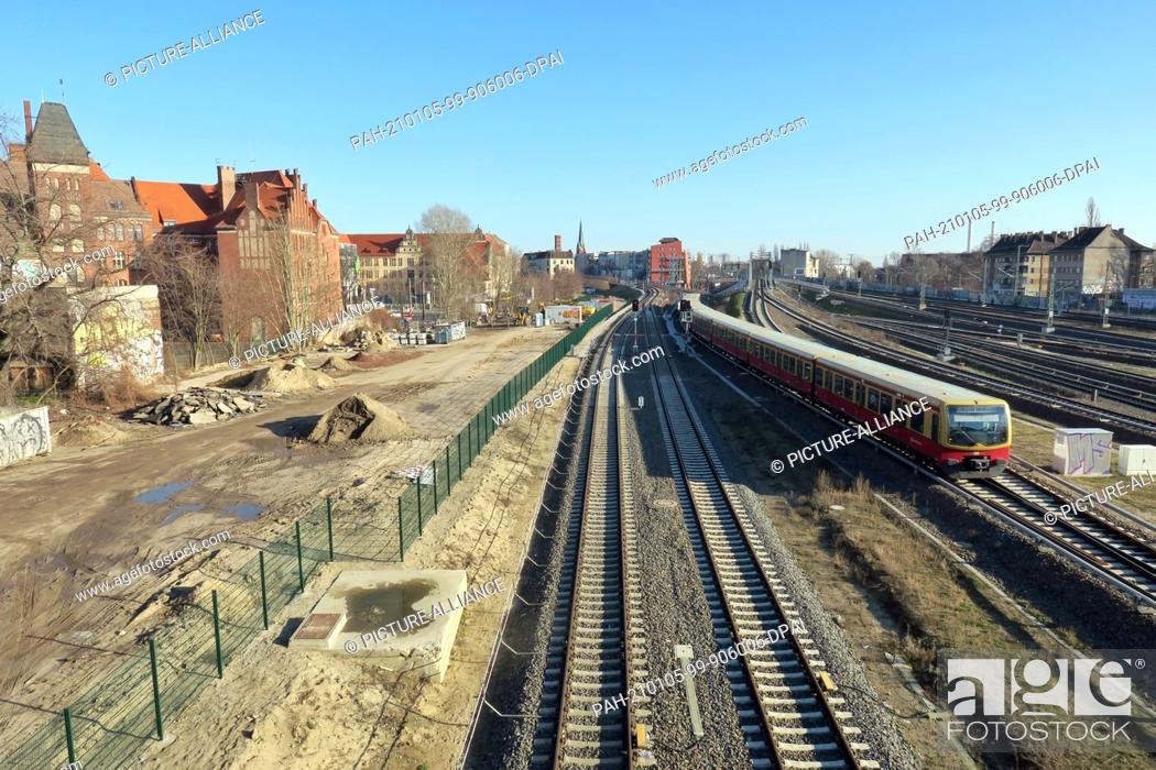Stock Photo: 08 February 2020, Berlin: An S-Bahn of the line S7 Potsdam runs near the station Ostkreuz. On the left is the leveled area for the future course of the tram.