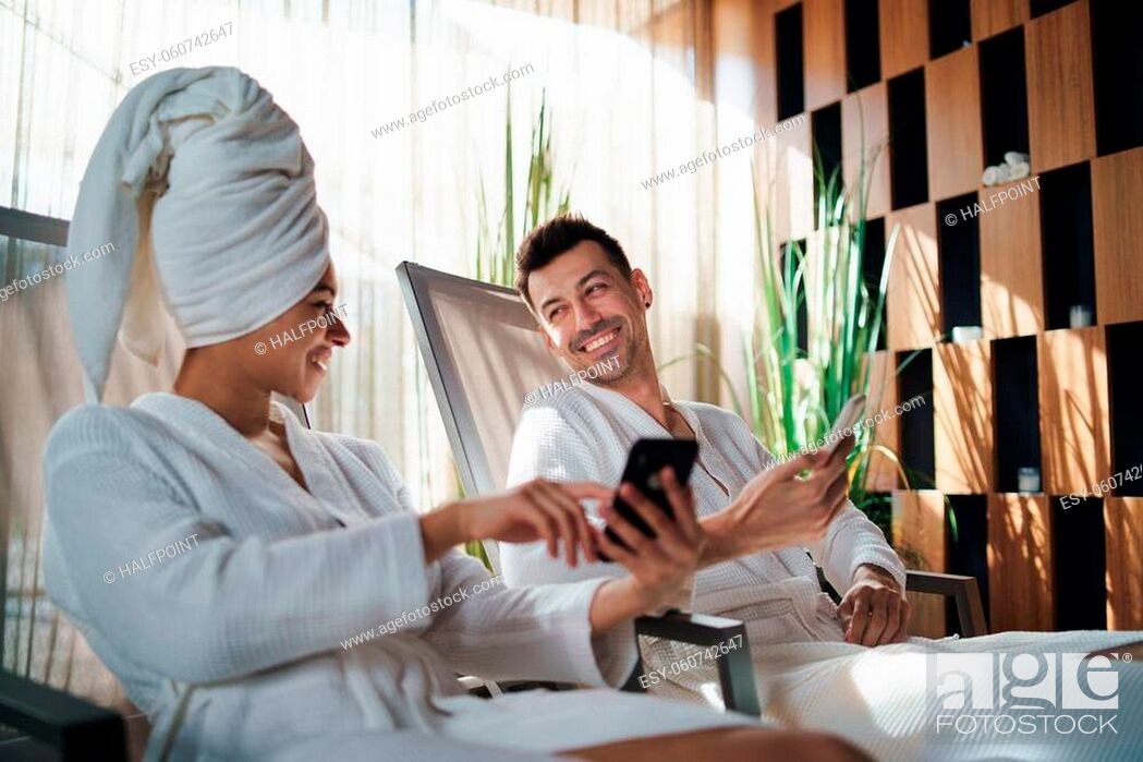 Stock Photo: A portrait of young couple relaxing in spa resort, using smartphone.
