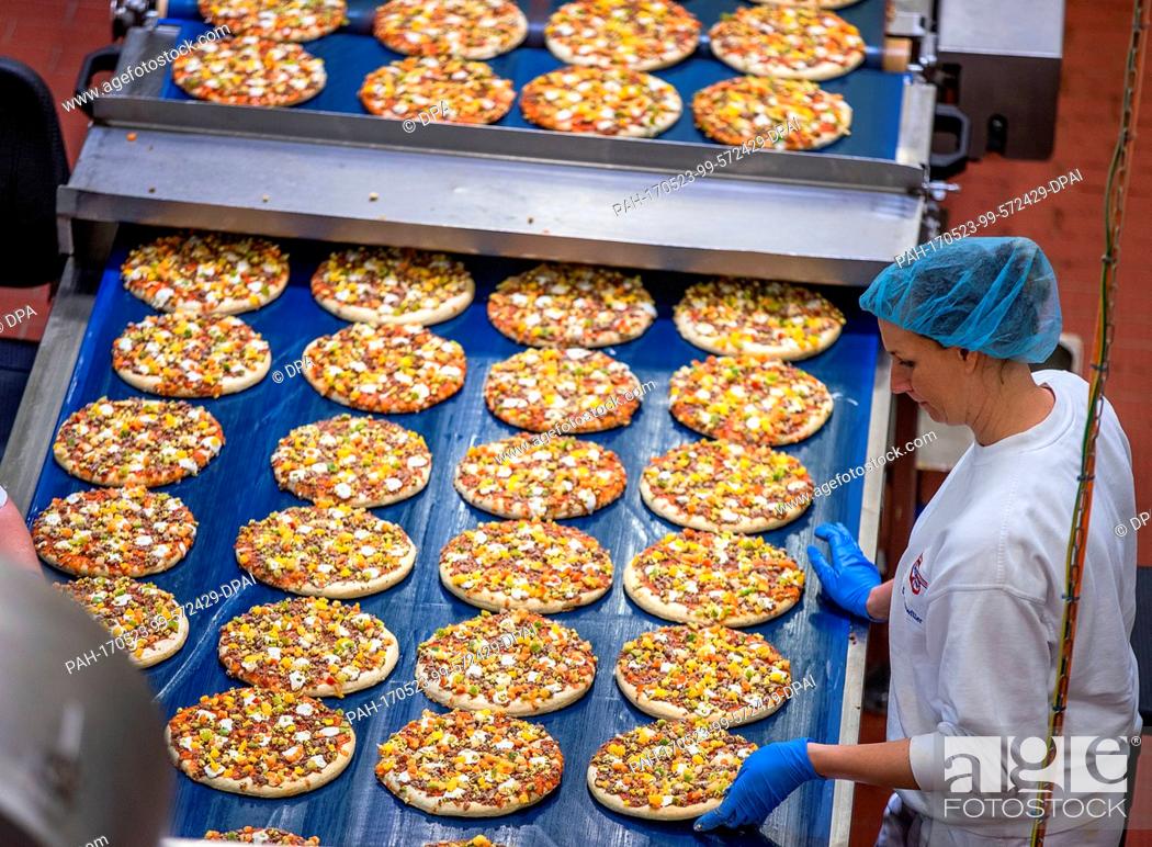 Stock Photo: Employees cover pizza crusts with vegetable pieces in the pizza factory of the Dr. Oetker company in Wittenburg, Germany, 23 May 2017.