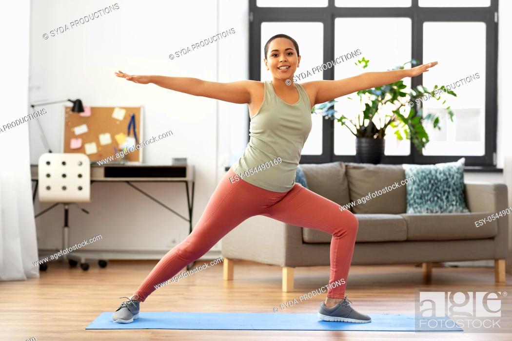 Stock Photo: african woman doing yoga warrior pose at home.