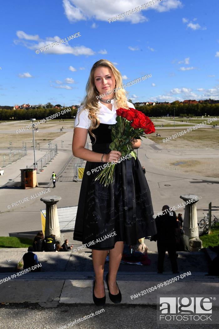 Stock Photo: 04 October 2020, Bavaria, Munich: The Munich child Viktoria Ostler stands in a black commemorative dirndl for the cancelled Wiesn 2020 with a bouquet of red.