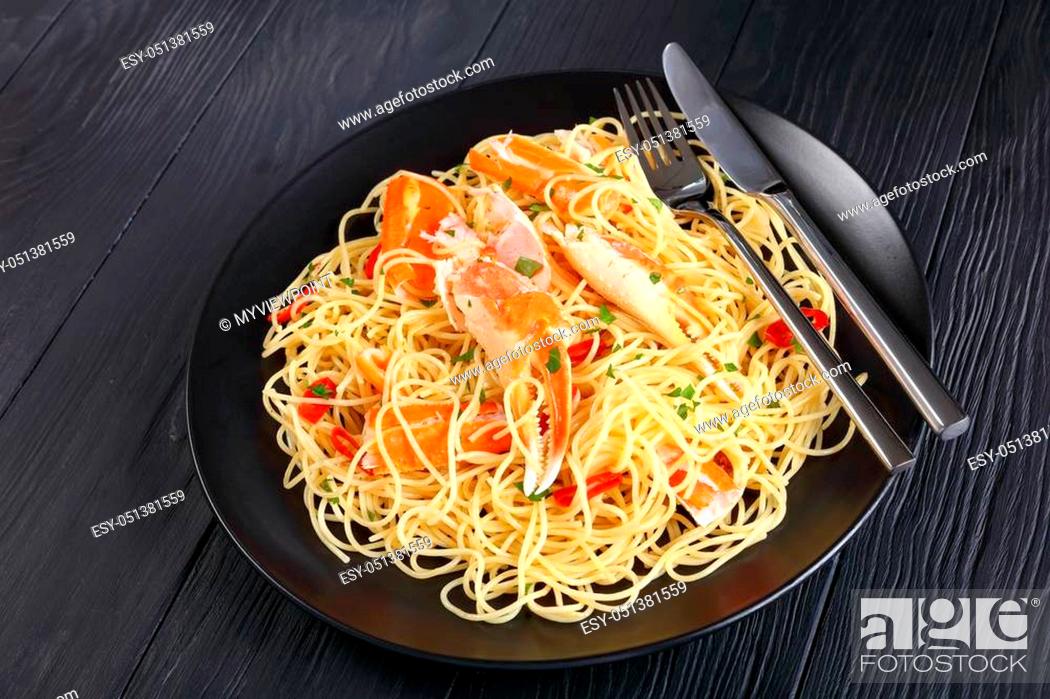 Stock Photo: close-up of spaghetti with cracked Crab in Spicy White Wine Sauce, sprinkled with finely chopped parsley and red chile served on black plate with fork and knife.