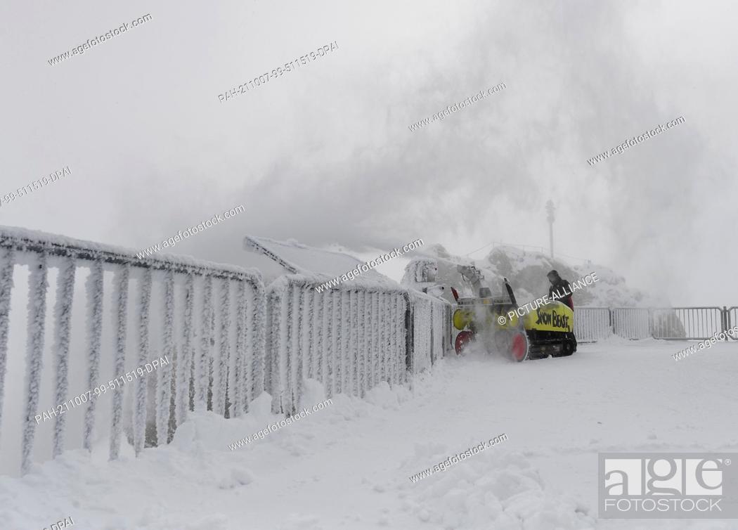 Stock Photo: 07 October 2021, Bavaria, Grainau: An employee clears the roof terrace of the Zugspitze mountain station with a snow blower.
