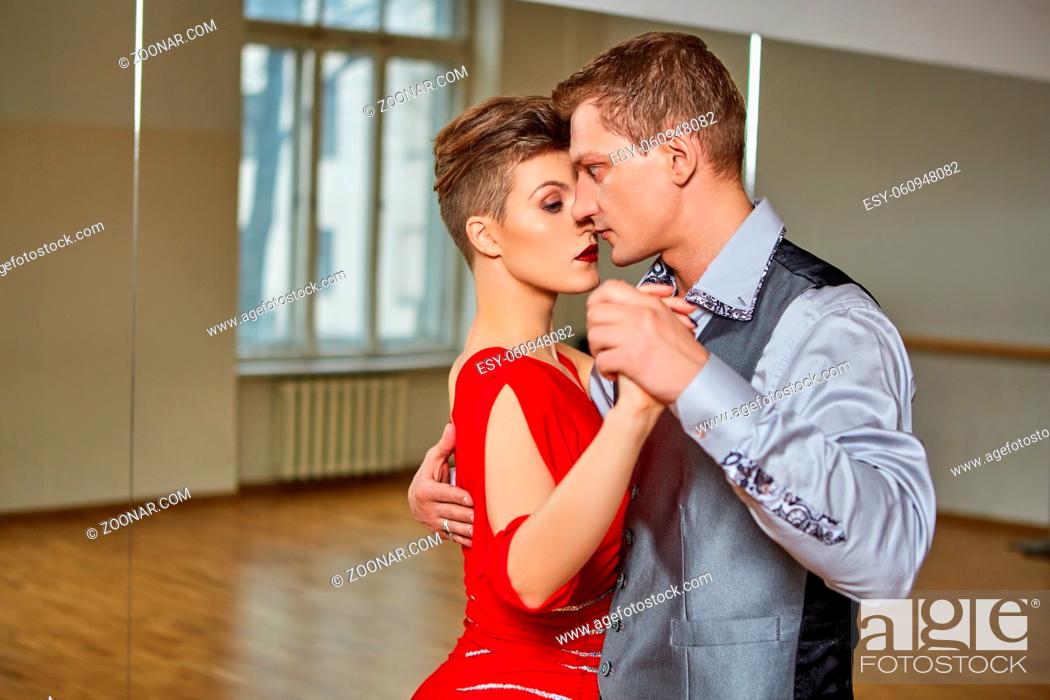 Stock Photo: beautiful couple dancing tango. young woman in red dress and man in suit practicing in dancing studio mirror room. copy space.
