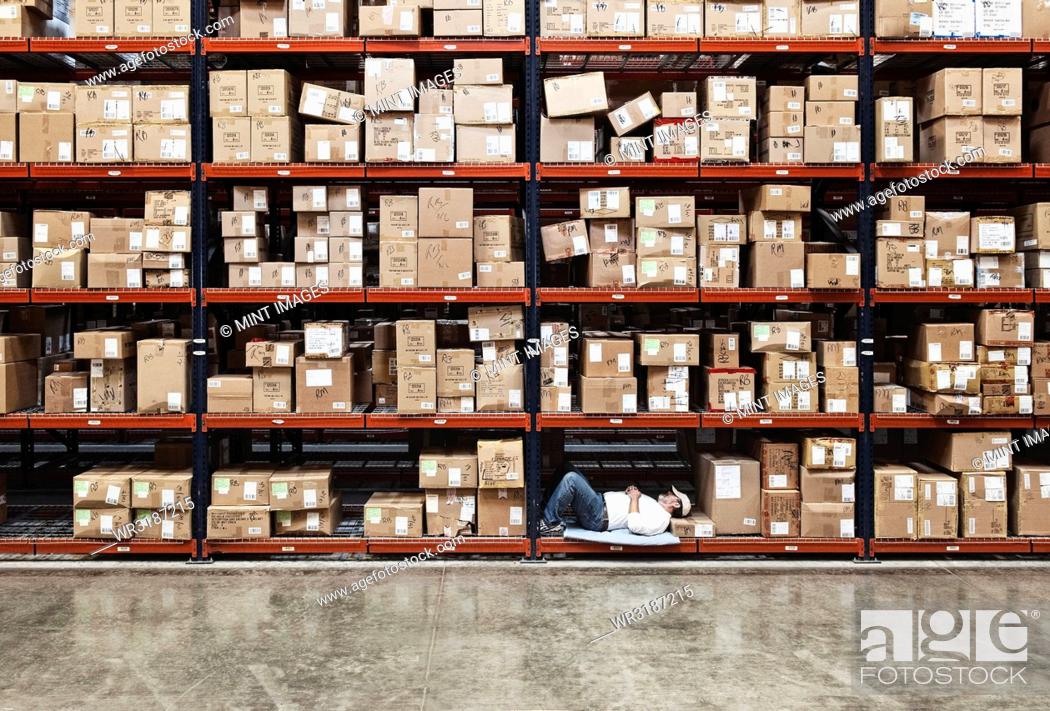 Stock Photo: Warehouse worker taking a break next to large racks of cardboard boxes holding product in a distribution warehouse.