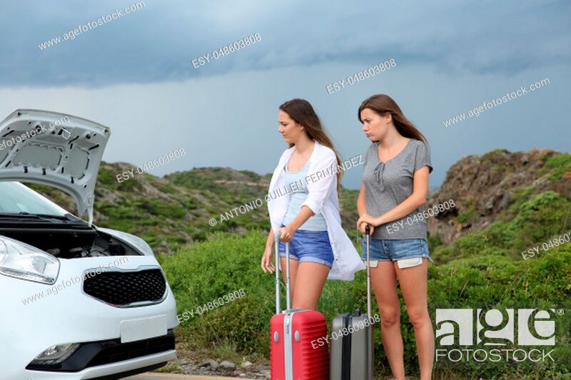 Stock Photo: Two frustrates tourists looking at the open hood of a breakdown car.
