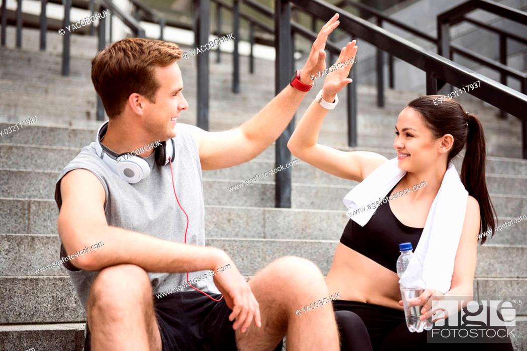 Stock Photo: Give me five. Contended young man giving five to lovely young woman while sitting on the stairs after doing sports.