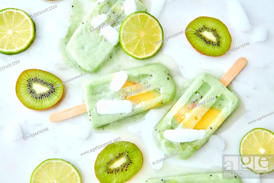 Imagen: Frozen fruit smoothies with a slice of mango presented on a gray background with pieces of ice, kiwi and lime. Healthy summer dessert. Flat lay.
