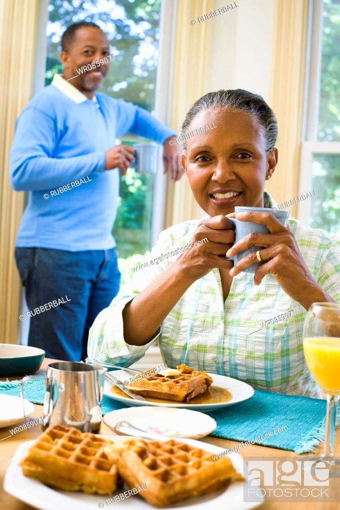Photo de stock: Portrait of a senior woman sitting at the breakfast table with a senior man standing behind her.