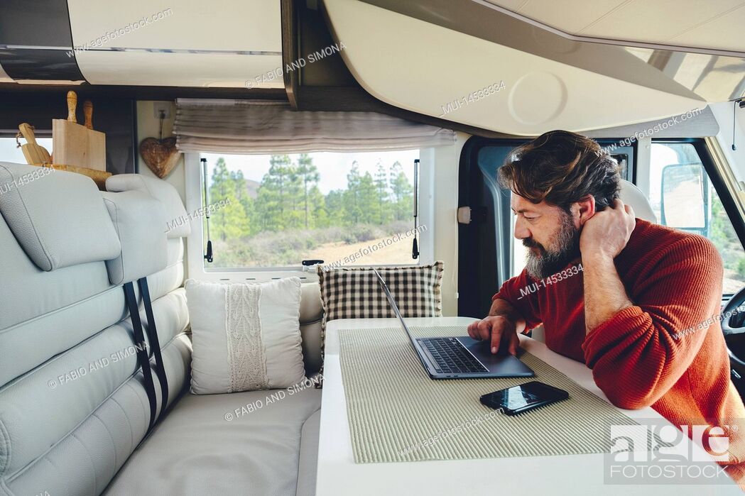 Stock Photo: Young modern adult man work on laptop computer in remote working and digital job lifestyle inside a modern and connected camper van with nature woods view.
