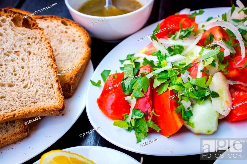 Imagen: Delicious fresh salad with tomato sauce sliced bread and cut lemon on a stylish black table.