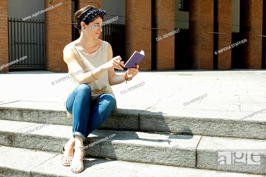 Stock Photo: Woman sitting on steps reading notebook, Milan, Italy.