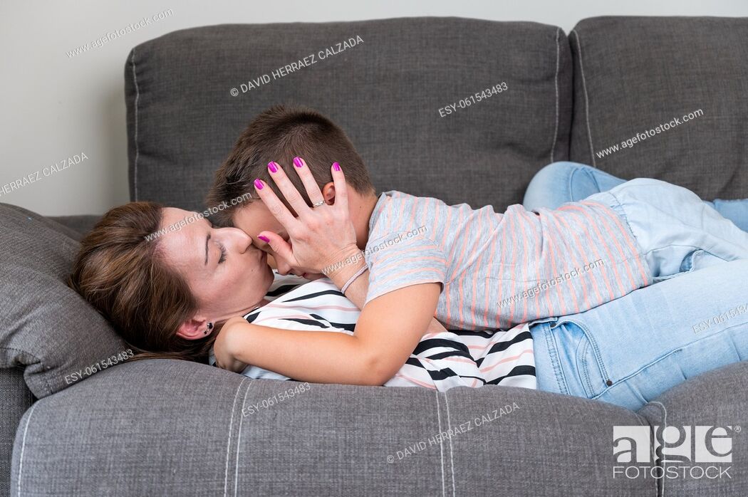Stock Photo: Woman lying on sofa kissing her little son in cheek. Mom with little boy joyfully spending time in cozy living room at home .