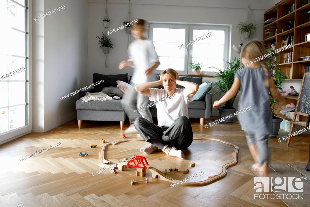 Stock Photo: Stressed out mother sitting in the middle of toys, while children are running around her.