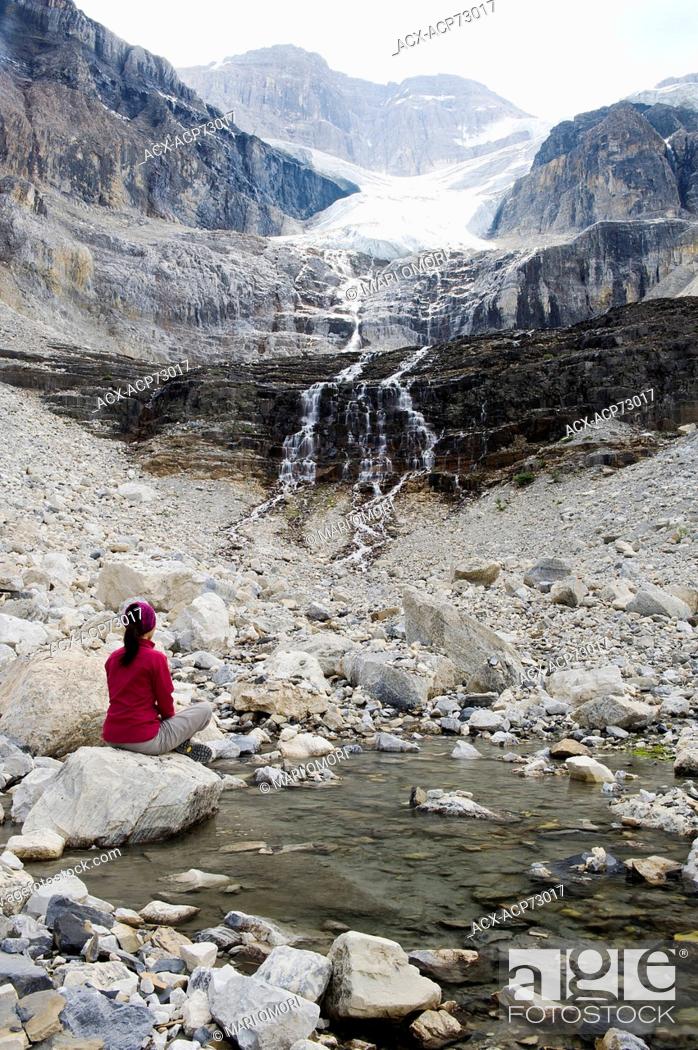Stock Photo: A hiker sits on a rock beside a pool of water fed by the Stanley Glacier. Smoke from nearby wildfire hang over the mountains. Model Release signed.