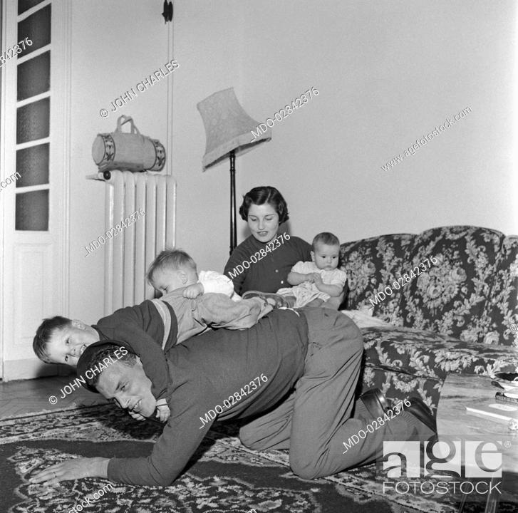 Stock Photo: Welsh football player forward of Juventus Football Club John Charles playing with his children beside his wife. Turin, 1957.