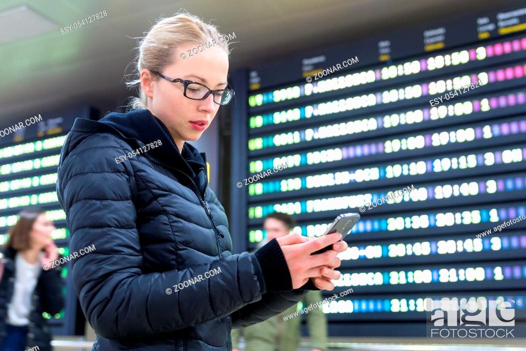 Stock Photo: Woman in international airport looking at smart phone app information and flight information board, checking her flight detailes.