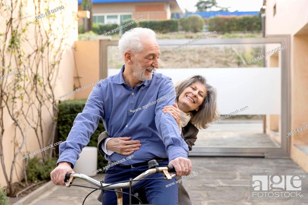 Stock Photo: Happy senior woman sitting with man riding bicycle.