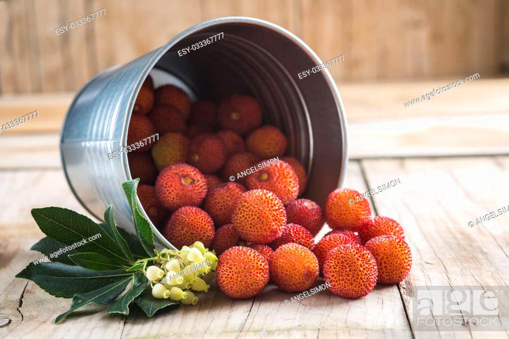 Stock Photo: Bucket with ripe arbutus unedo fruits, leaves and flowers on a wooden background.